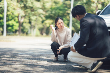Car Accident Report: A concerned woman discusses details with an insurance adjuster near a damaged...