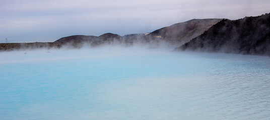 Blue water and lava rock mountains at the Blue Lagoon in Grindavik Iceland during a cloudy day