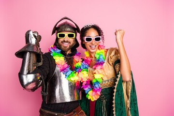 Playful couple in medieval-themed costumes posing energetically with regal and modern styles against a pink backdrop