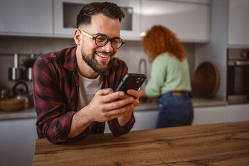 portrait of adult man stand and use mobile phone in the kitchen