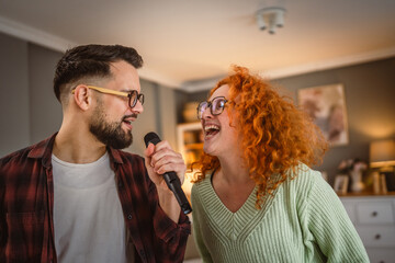 cheerful couple have a home party sing on microphone and dance at home