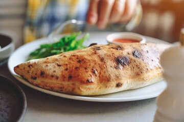 Enjoying freshly baked calzone with salad and dipping sauce at cozy restaurant
