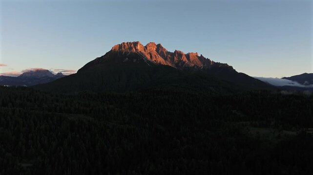 Sunrise over the Dolomites with vibrant hues on the Antelao and Cridola peaks, framed by dense alpine forests below. Captured near Danta village, Italy. Hiking in Italy. Aerial 4k video.