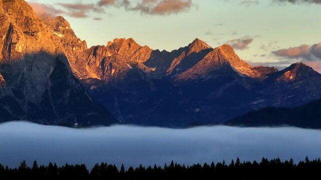 Sunrise over the Dolomites with vibrant hues on the Antelao and Cridola peaks, framed by dense alpine forests below. Captured near Danta village, Italy. Hiking in Italy. Aerial 4k video.