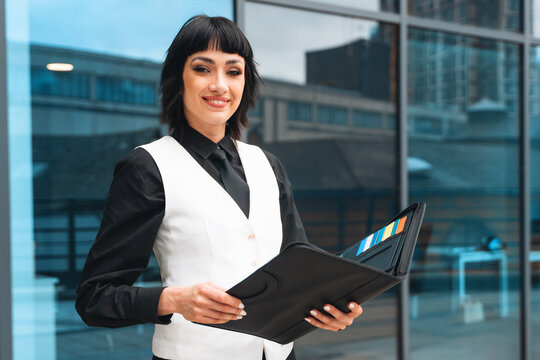 Professional woman holding a portfolio outside a modern building during daylight