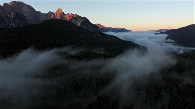 A mist-filled valley in the Dolomites at sunrise, with sunlight highlighting the peaks and dense alpine forest below. Taken near Danta village. Aerial photo with Dolomites. Hike in Italy. 4k video