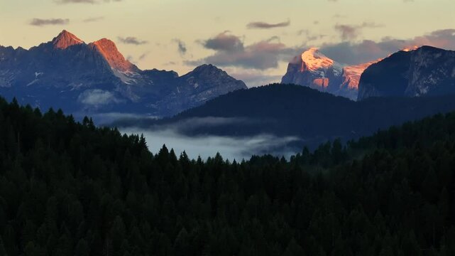 A mist-filled valley in the Dolomites at sunrise, with sunlight highlighting the peaks and dense alpine forest below. Taken near Danta village. Aerial photo with Dolomites. Hike in Italy. 4k video