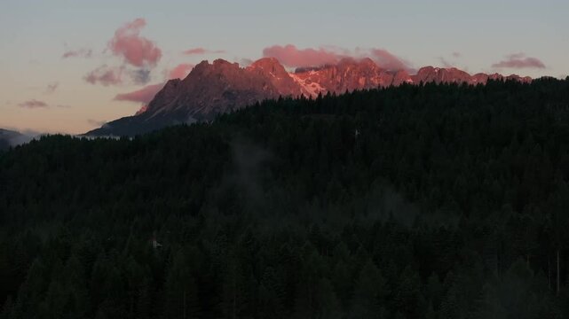 Sunrise over the Dolomites with vibrant hues on the Antelao and Cridola peaks, framed by dense alpine forests below. Captured near Danta village, Italy. Hiking in Italy. Aerial 4k video.