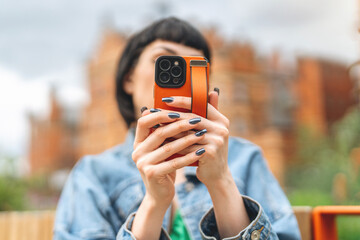 Person holding a smartphone while sitting outdoors on a sunny day in an urban setting