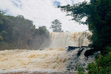 Cascading water of Bou Sra waterfall with mist and lush vegetation against an overcast sky in...