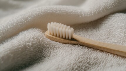 Close-up of a toothbrush resting on a white towel. the toothbrush has a wooden handle and white bristles. the bristles are arranged in a circular pattern and appear to be soft and fluffy.