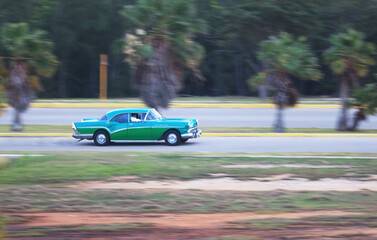 A vintage car drives along a country road on the Caribbean island of Cuba, Caribbean, Central America..