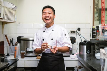 Happy face of a young professional Asian chef's laughter in the commercial Chinese restaurant kitchen