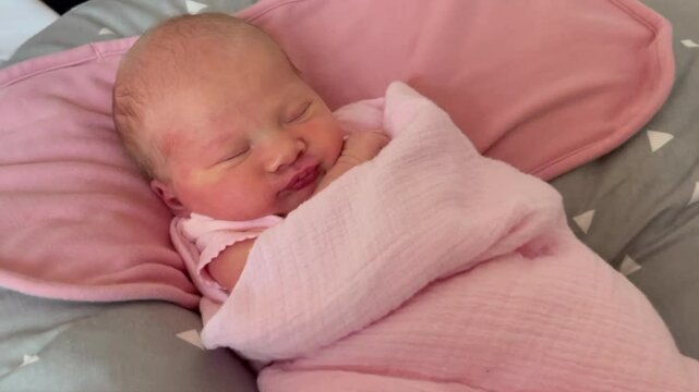 Close-up of a newborn baby lying in the lounger swaddled. The baby is two weeks old and shows typical features of a newborn baby: flaking skin and pimples, slight redness of the face. 