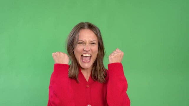 Young woman in red shirt counting one two, and three on  fingers and celebrating success with fists raised against green background 