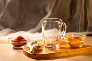 Empty transparent cup on wooden tray with turmeric and chili species. Mock up for design. Served table. Preparation for making drink