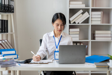 Focused Work: A young businesswoman sits at her desk, deeply engrossed in her work. She's using a...
