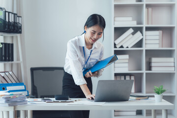 Focused and Ready: A confident young businesswoman with a friendly smile stands beside her desk,...