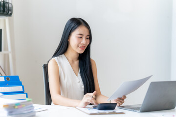 Focused Accountant: A young, smiling businesswoman sits at her desk, meticulously reviewing...