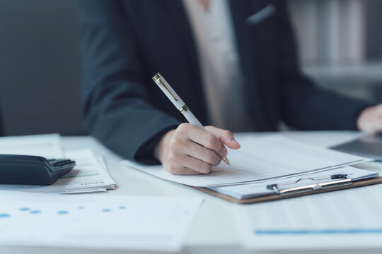 Businesswoman Signing Documents: Close-up of a businesswoman's hand signing important documents on a clipboard, showcasing professionalism and attention to detail in a modern office setting.  