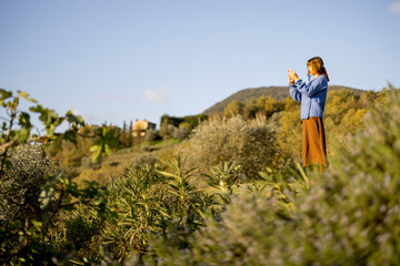 A woman taking a photo of the scenic Tuscan countryside, surrounded by lush greenery and rolling...