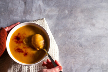 Woman tasting pumpkin soup with paprika spices and cream on white table. Kitchen napkin. Flat lay with copy space. Cream soup. Concept of tasty healthy food.
