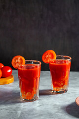 Two Bloody Mary cocktails in glass served with tomato slice and salt on dark background. Red cocktail. Alternative taste. Dirty dump drink