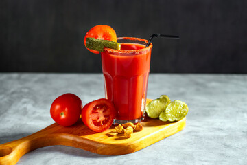 Bloody Mary cocktail in glass served with tomatoes and pickles on grey stoned surface. Red cocktail. Alternative taste. Dirty dump drink