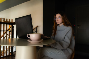Young woman working on her laptop, drinking coffee at a cafe. Ideal for concepts of freelance, remote work, or study in a cozy cafe setting.