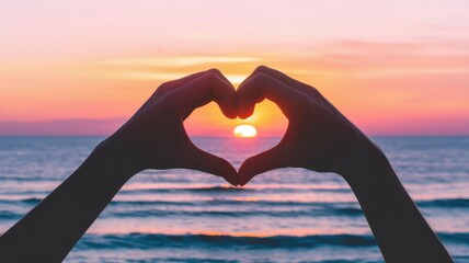 A pair of hands forming a heart shape against a stunning sunset at the beach, creating a romantic and serene atmosphere.