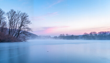 Fototapeta premium Iced-over river landscape at dawn with morning mist, serene beauty