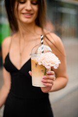 Coffee and pink flower in the hand of a smiling girl in a black dress