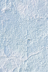 A detailed close-up of a white plaster wall with a rough, uneven texture, showcasing cracks and natural imperfections in the surface.  
