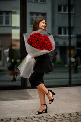 Gorgeous bouquet of red roses in hands of smiling girl in a black midi dress