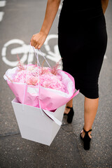 Beautiful bouquet in a gift bag is held by a young slender woman