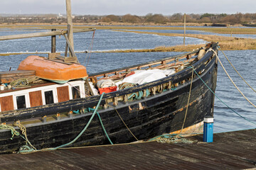 Bow Section of Weathered Wooden Fishing Boat Moored Tied-Up at Harbour Dock in Coastal Landscape