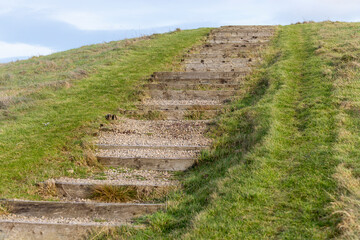 Obraz premium Wooden Sleeper and Gravel Steps Leading Up Grassy Slope Mound or Hill Concept for Journey, Struggle, Achievement, Ambition, Progression, and Success