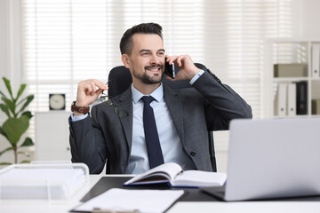 Happy banker talking on smartphone at table in office