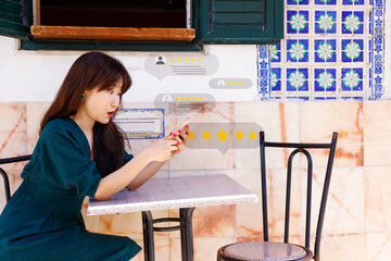 asian businesswoman sitting at an outdoor café table engaged in reading or responding to reviews....
