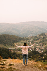 A person stands with arms wide open, fully enjoying a breathtaking panoramic view of majestic mountains