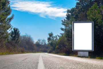 White vertical advertising poster on the way. Billboard on the side of the asphalt forest road....