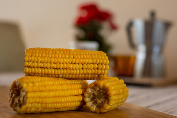 corn cobs on wooden table with coffee in background and red flower