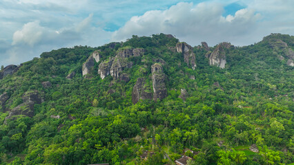 Fototapeta premium Panorama of the Nglanggeran Ancient Volcano ecotourism area in the afternoon using a drone. Aerial photo of an ancient rock mountain covered with majestic lush trees