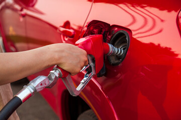 Selective focus view of the arm of a young man pumping gas into a red car