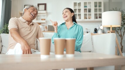 Happy elderly couple enjoying a ball toss game together at home, practicing coordination and cognitive skills for healthy aging. Grandfather and grandmother throwing ping pong in the bowl. Myrmidon.