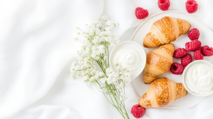 Golden croissants served with fresh raspberries, cream, and flowers on a bright white setting, ideal for a delicious brunch.