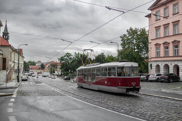 Naklejka premium Old vintage tourist tram comes through the alley of a Prague city in an autumn day. Electric transport connection. Prague tram network is third largest in a world. Retro historic electro transport