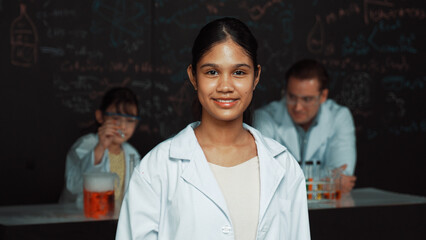 Girl looking at camera with arm folded while people doing experiment at laboratory. Cute student...