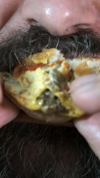 Adult bearded man eating a nourishing hamburger. Junk food. Close-up. Selective focus.