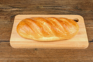 Flavorful whole loaf of white bread on a wooden cutting board in full sharpness.